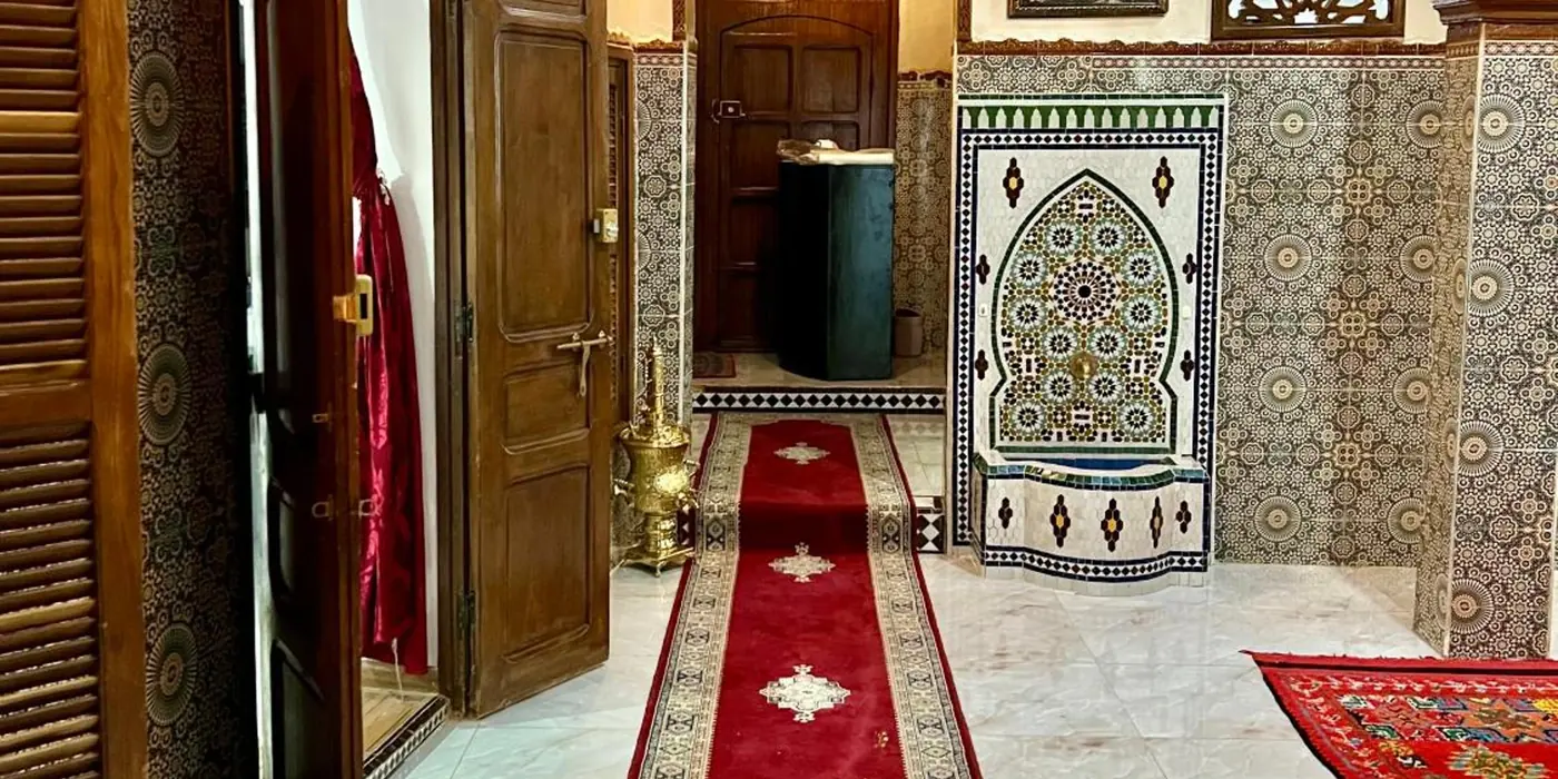 Le couloir de l’entrée, la fontaine de zellige et les tapis rouges