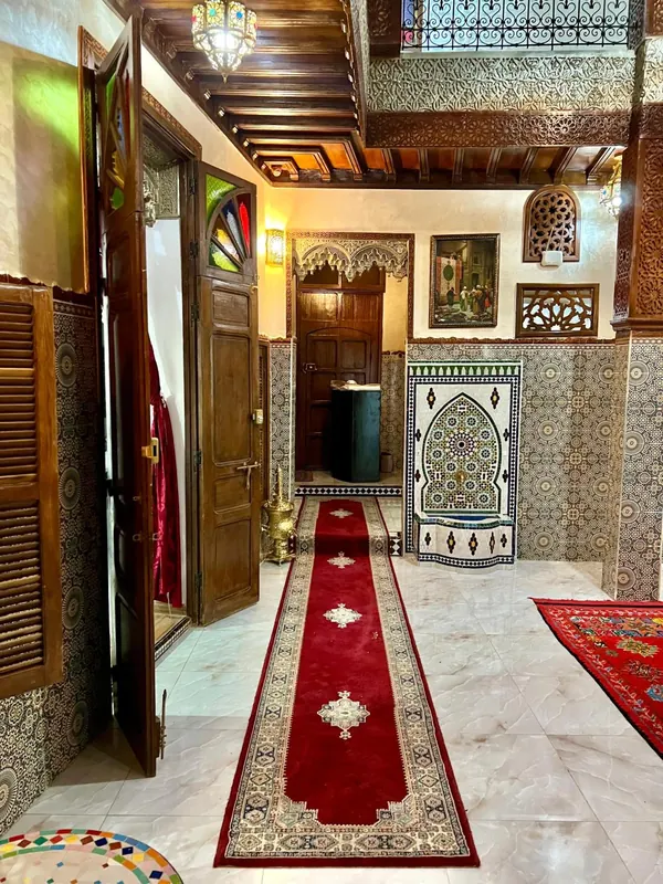 Le couloir de l’entrée, la fontaine de zellige et les tapis rouges
