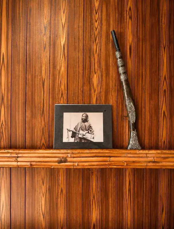 Une photographie ancienne et un fusil, sur un mur de bois